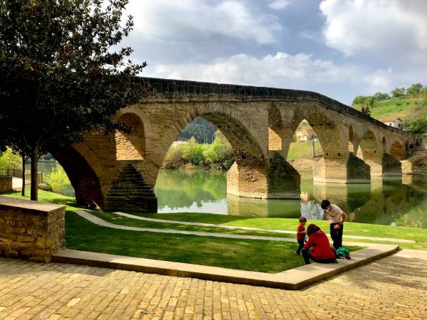 Puente románico sobre el río Arga y unas personas en un jardín de la orilla